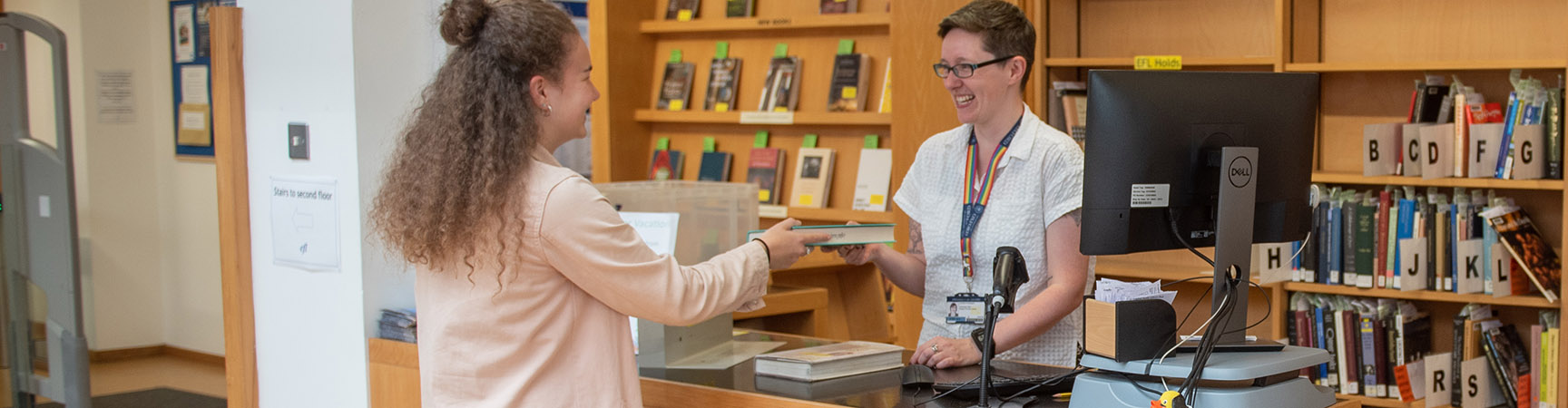 A student handing a book to a librarian at the information desk