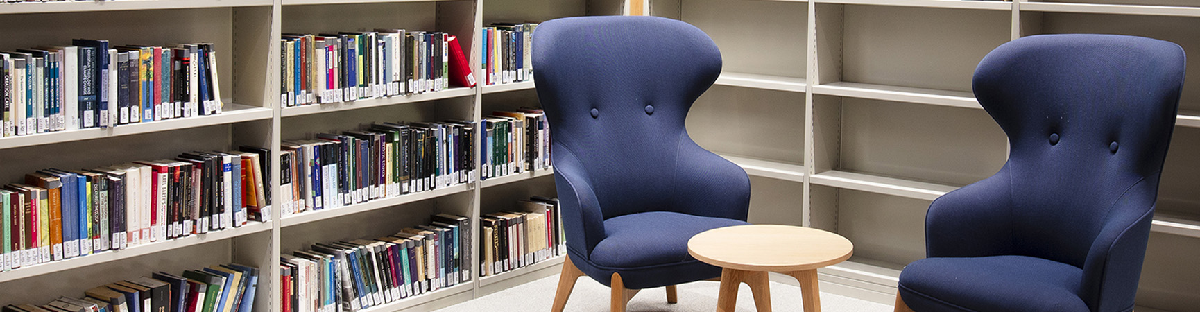 Two soft blue armchairs and a small wooden table in front of bookshelves