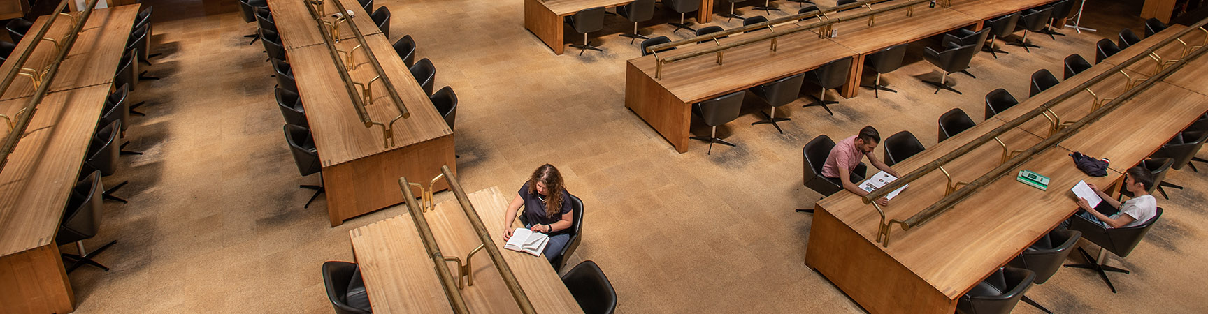 A birdseye view six long wooden desks, four students are scattered around reading at them