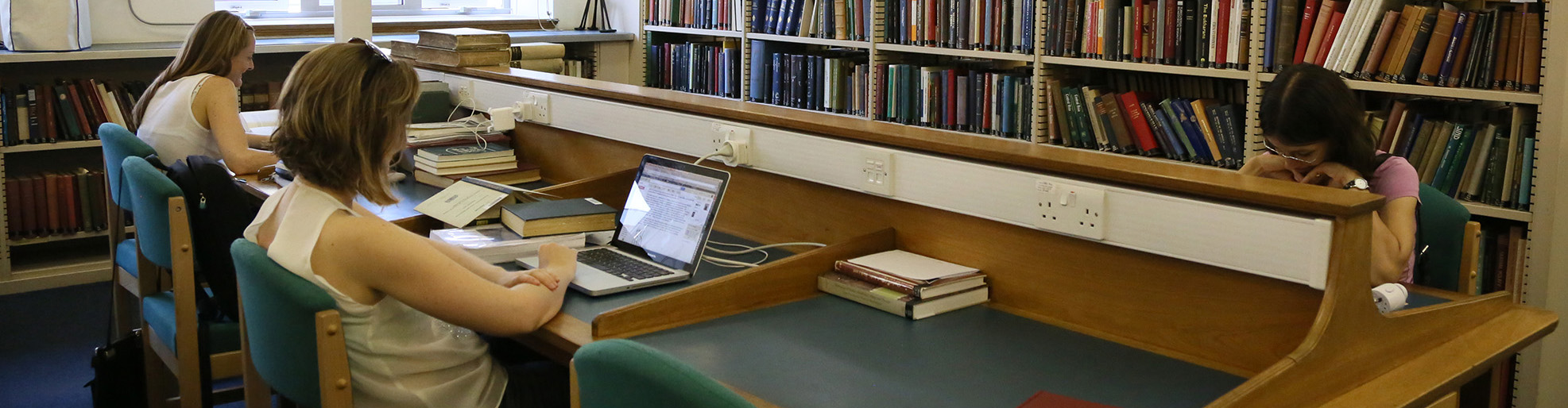 Two students sit next to each other at a three-seater library desk