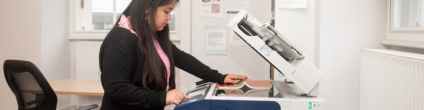 A student holds a book facedown on a scanner