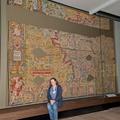 A woman sits on a bench in front of a floor to ceiling glass display case with the tapestry on display