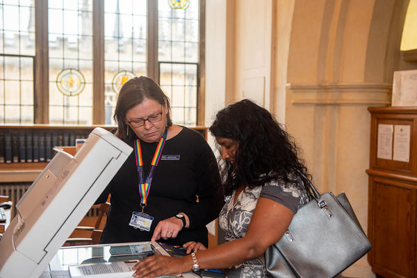 A member of library staff helps a library user to scan a book on a library scanner