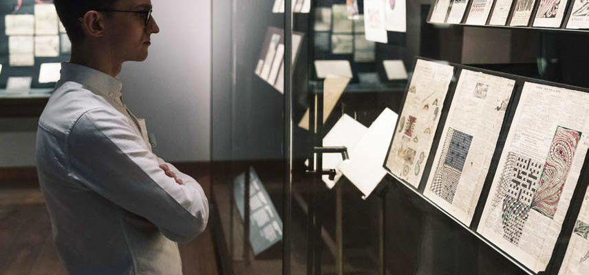 A view of an exhibition: a person looks at a glass display case - with 2D material within it
